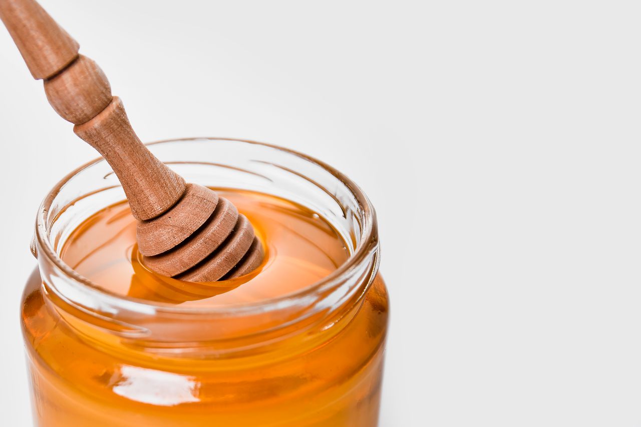 The Art of Drawing Readers In: Your attractive post title goes here Glass jar of honey with a wooden dipper, set against a white background. Perfect for food and kitchen-related content.